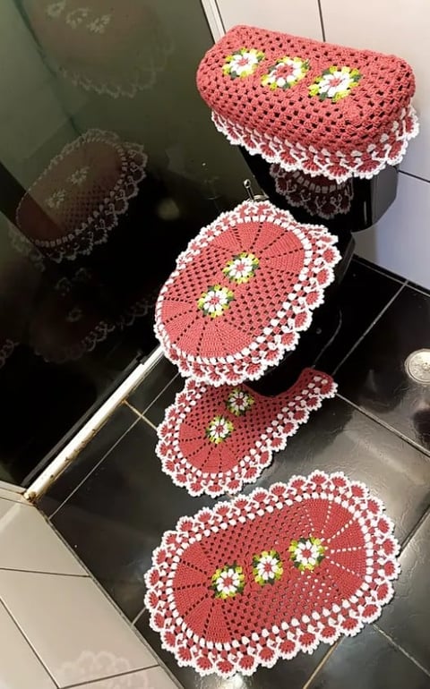 Collection of crocheted doilies with red mesh, white lace edges, and embroidered white daisy flowers arranged on a black stovetop